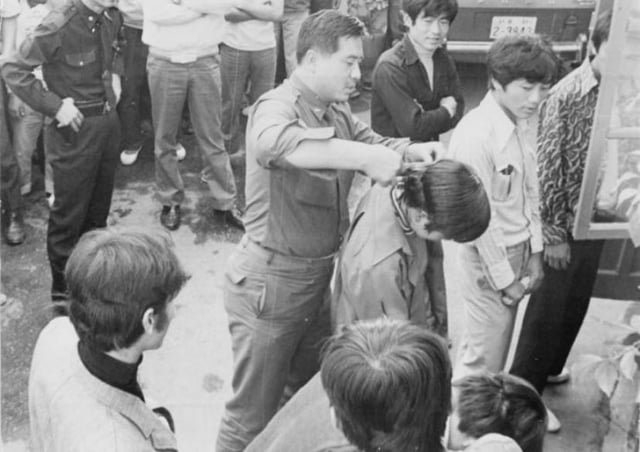 A South Korean soldier forcibly cuts a young man’s hair in front of others during a nationwide crackdown on men with long hair and women wearing short skirts in South Korea – 1970s