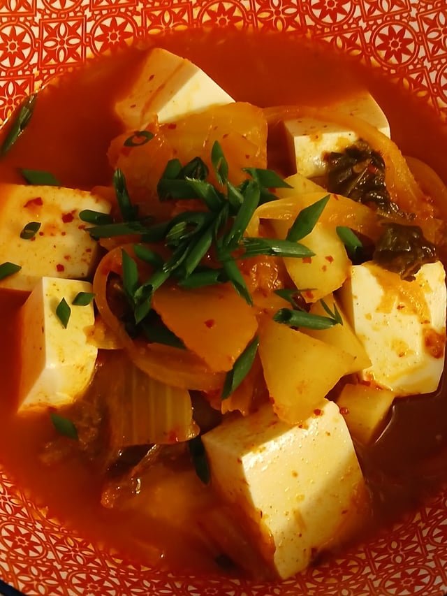 Kimchi Jjigae with soft tofu and lots of chives ontop.